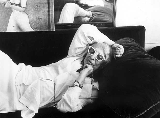 Imagen en blanco y negro de Silvina Ocampo en su vejez, recostada en un sillón oscuro. Viste ropa clara y gafas blancas de marco grueso. Apoya un brazo sobre la cabeza y el otro en el mentón, en actitud reflexiva. Detrás se observa un espejo y una pintura en la pared.