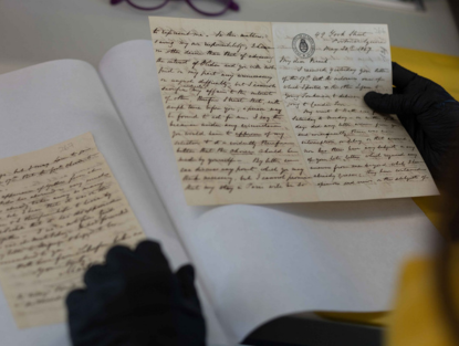Manos con guantes negros revisando manuscritos antiguos.