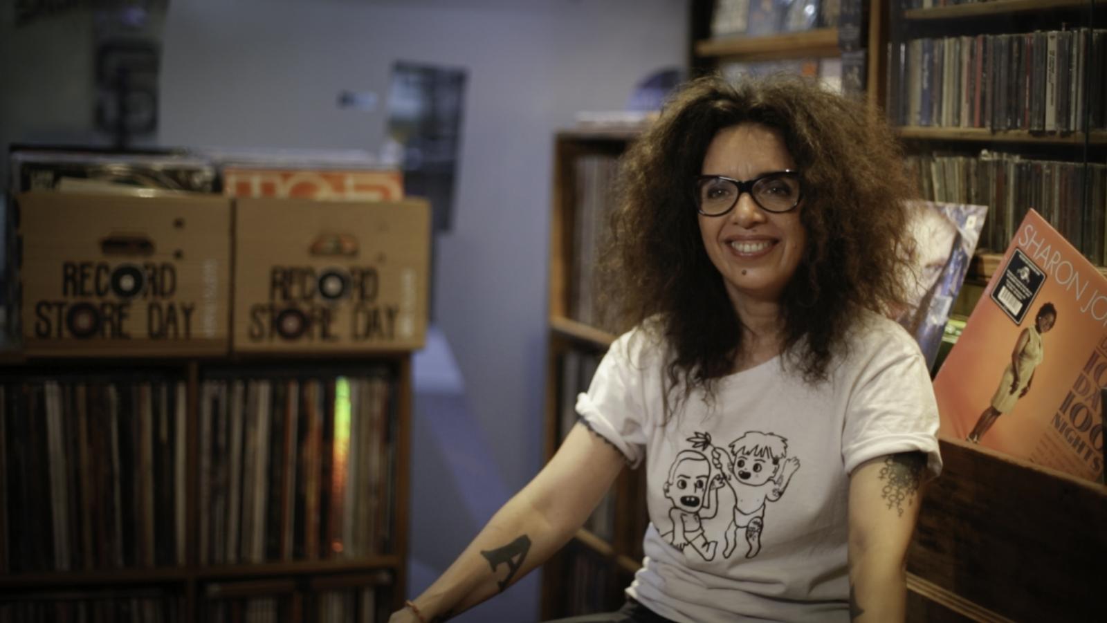 Una persona sentada en un sillón con una biblioteca de fondo.