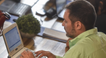 la imagen muestra a un docente hombre en un escritorio mirando una netbook.