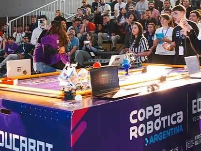 Mesa con robots de la competencia, público y participantes