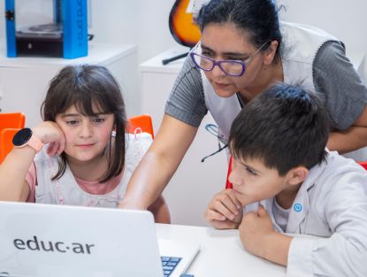Aniversario 25 educar. Docente con 2 alumnos frente a computadora