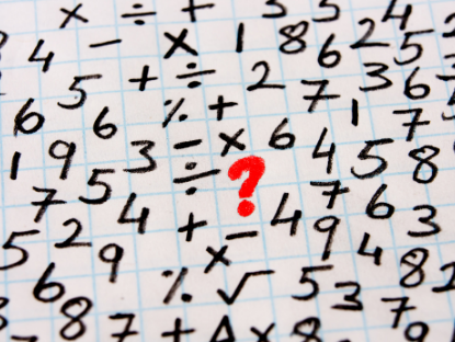 Sobre un papel cuadriculado aparecen números y signos matemáticos distribuidos al azar. En el centro un centro de interrogación de color rojo.