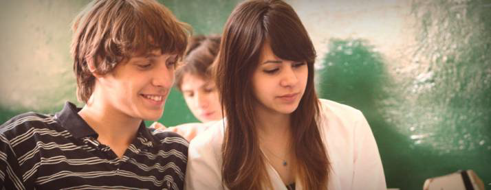 Estudiantes adolescentes con un pizarrón verde de fondo.