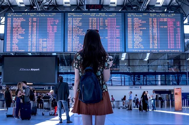la imagen muestra a una joven en un aeropuerto mirando el tablero de vuelos