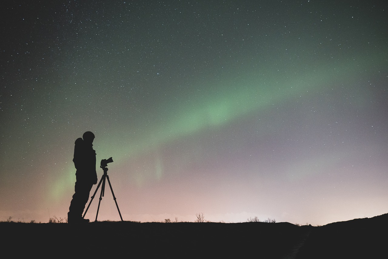 la imagen muestra una aurora boreal y un hombre con un telescopio observándola.
