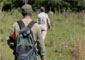Dos biólogos de espaldas caminando en la vegetación. Uno de ellos lleva gorra y una mochila.
