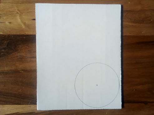 Trazado en color negro de un círculo en la esquina inferior derecha de un pedazo de cartón.