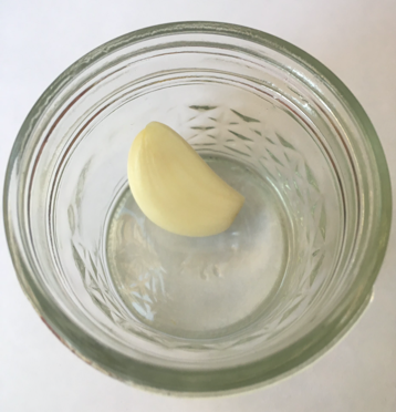 Diente de ajo pelado adentro de un vaso de vidrio.