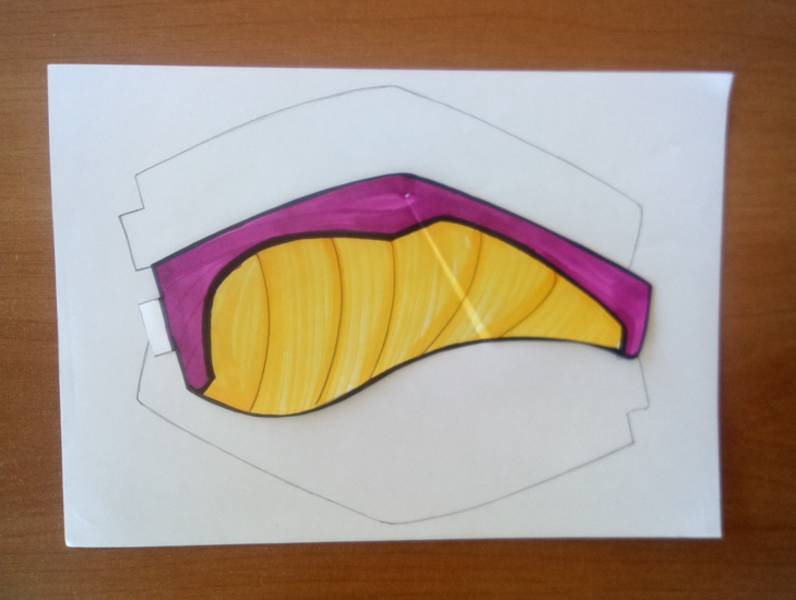 Una hoja con las alas del dragón dibujadas. Encima de la hoja, hay un ala con la cara interior ya coloreada y recortada.