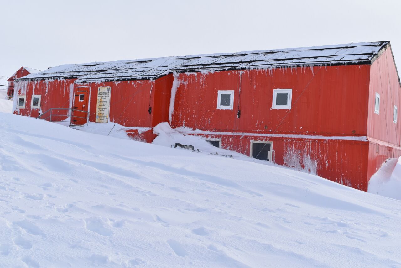 Edificio de la Escuela Provincial 38. Tiene techo negro a dos aguas, paredes rojas y pequeñas ventanas. Hay nieve alrededor y en el techo.