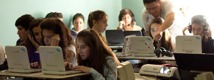 Grupo de studiantes en una capacitación utilizando netbooks y auriculares. Los acompaña un facilitador.