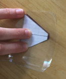 Una mano sosteniendo el molde de papel con forma de trapecio sobre un recorte de plástico transparente.