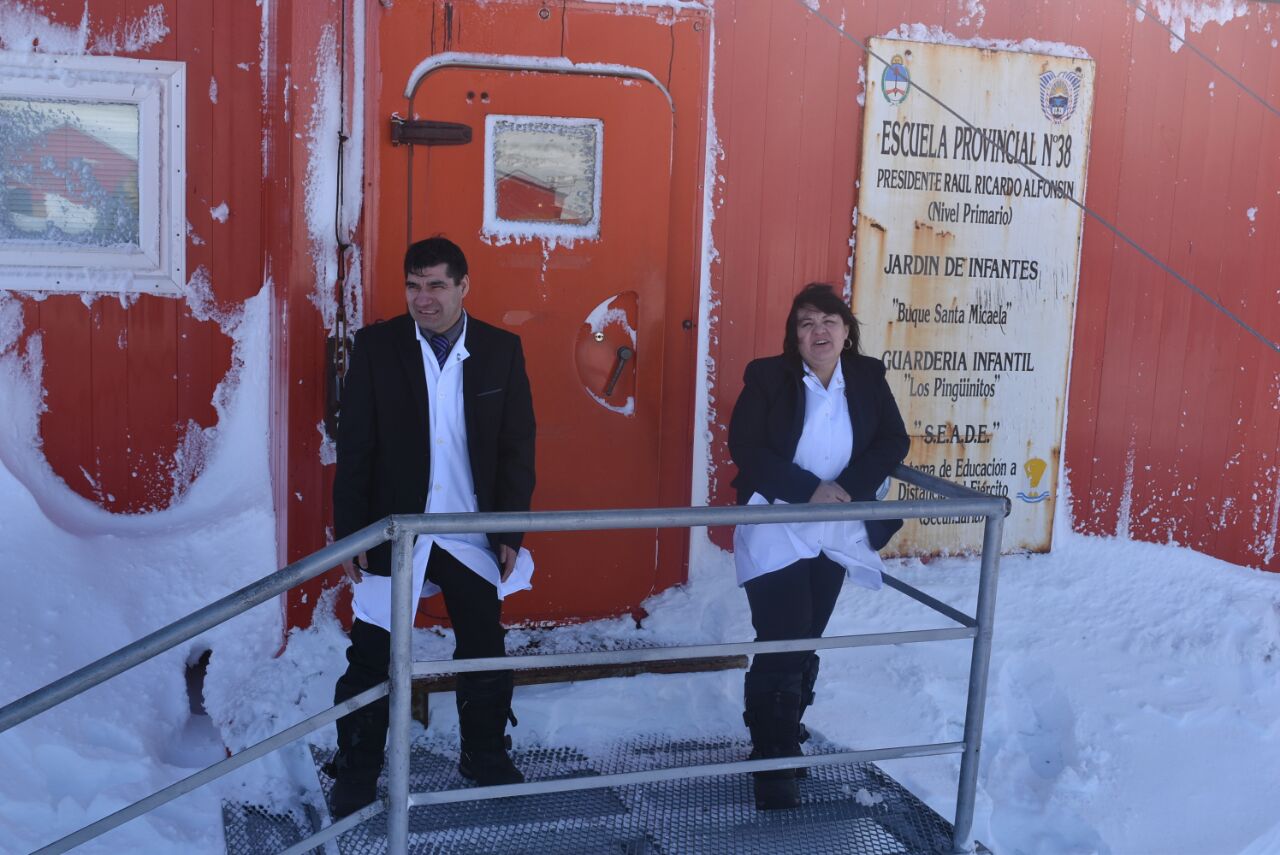 Escuela de paredes rojas en la nieve. En la puerta, Julio Palavecino y Griselda Ramírez resisten el viento. Llevan delantales blancos bajo el abrigo.