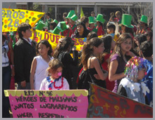 Personas adultas, jóvenes, niños y niñas en un festejo popular. Algunos tienen galeras verdes; otros, collares coloridos y nariz de payaso. Sostienen pancartas y estandartes coloridos.