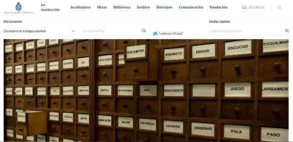 Página de inicio del sitio web de la Real Academia Española. Está el logo de la RAE, el menú de opciones y buscadores de términos en varios diccionarios y de dudas rápidas. Abajo se ve un gran fichero de madera con cajones para cada término del diccionario.