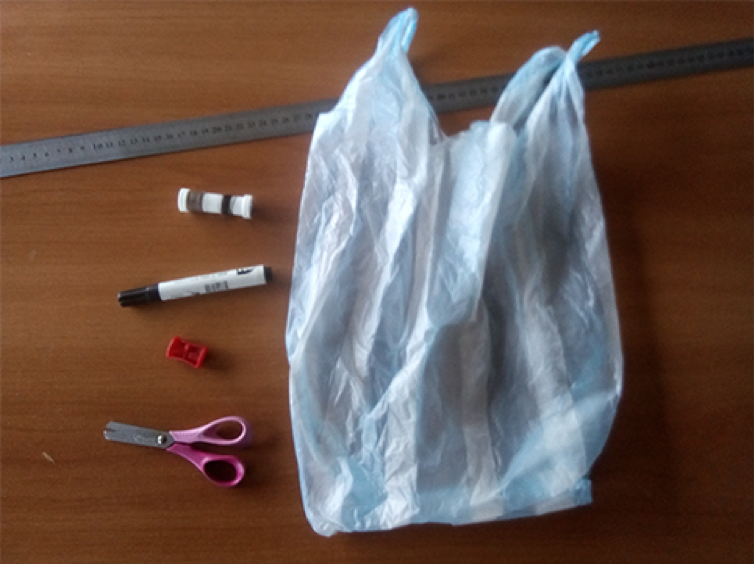 Una bolsa de plástico, una tijera, un sacapuntas, un marcador, hilo y una regla dispuestos sobre una mesa.