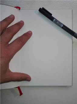 Una mano izquierda sosteniendo una hoja de papel sobre la mesa y un marcador apoyado en la hoja. 