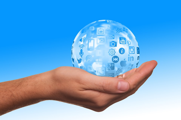 Una mano sostiene una bola transparente, como un pequeño mundo, con logos de redes sociales y empresas de tecnología en su superficie en tono celeste.